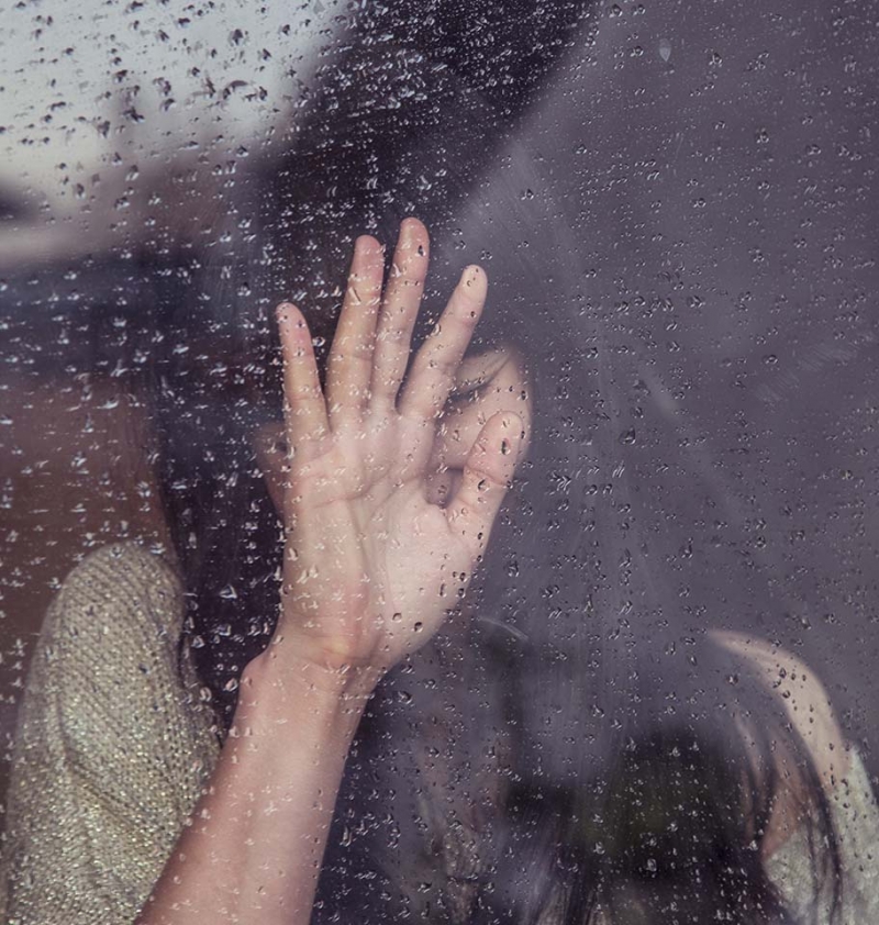 Femme posant la main sur une vitre sous la pluie